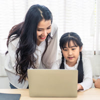Happy Asian mother and daughter using a laptop computer for elementary school remote learning