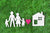 White paper cut outs of a family, white house and red heart arranged on a green turf background