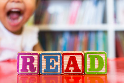 Block letters spelling read on a red table in front of an excited child