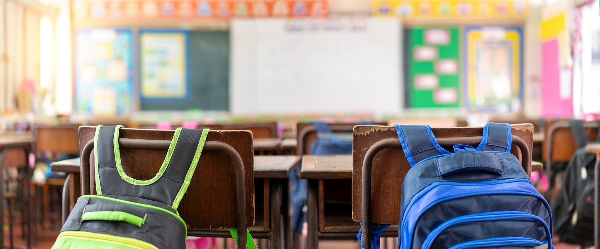 Two backpacks hanging on chairs in an empty classroom