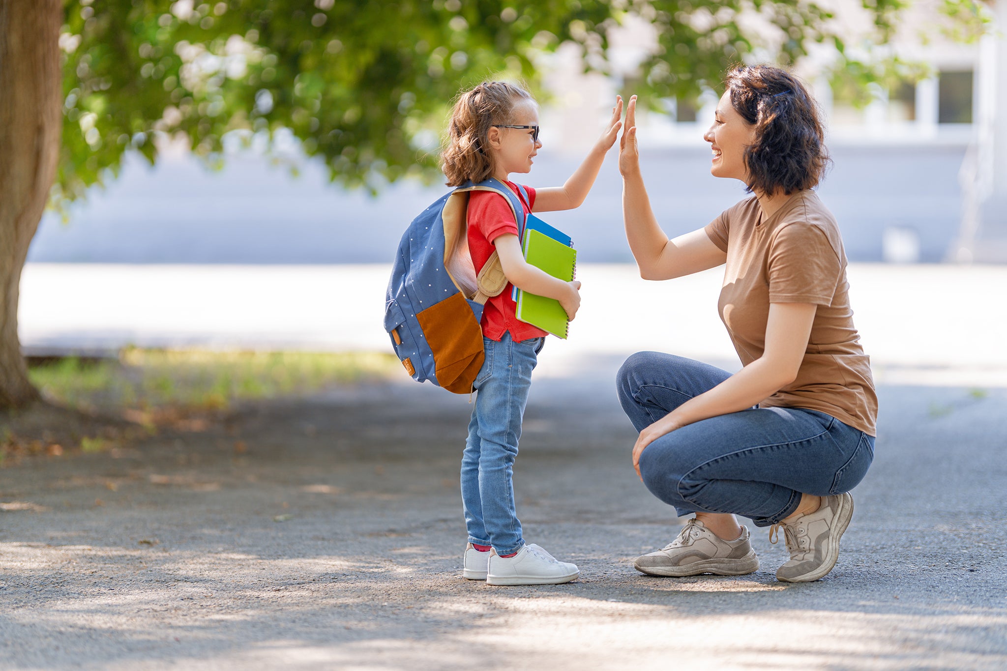 Crouching woman giving a high five to a young girl wearing a backpack