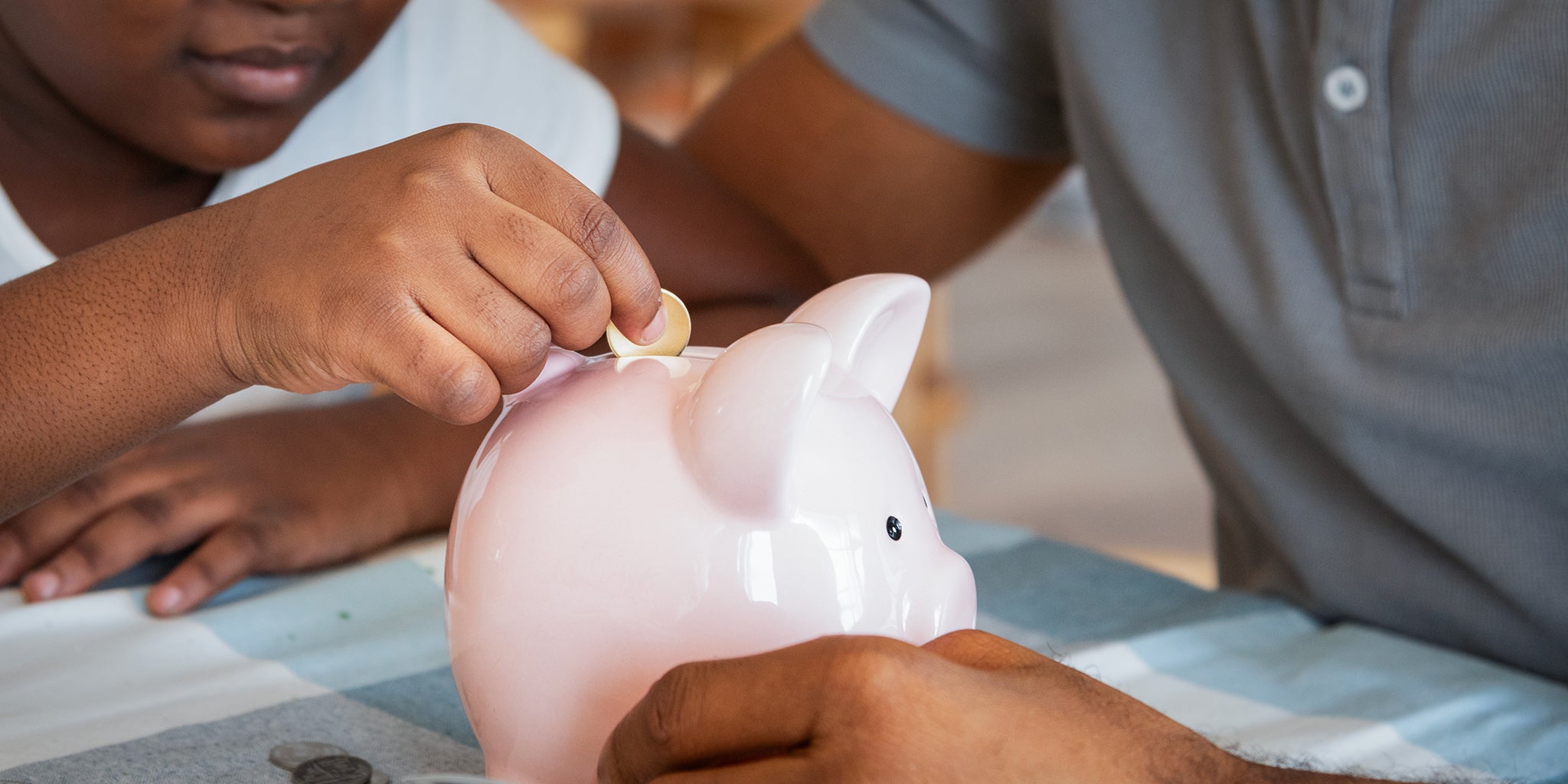 Child putting a coin into a piggy bank next to father