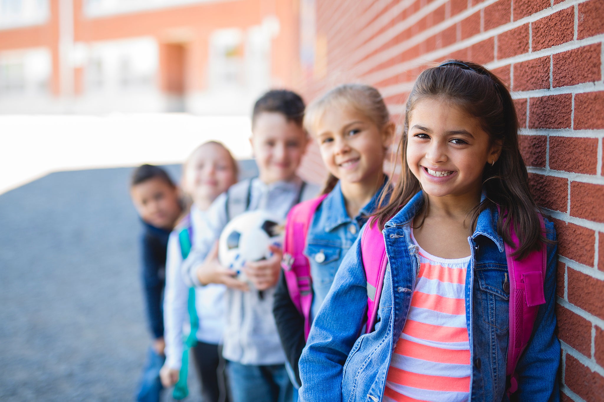 Group of diverse elementary school children leaning against a brick wall, smiling