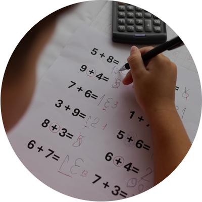 Hand writing math equations on a piece of paper with a calculator in the background.