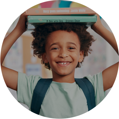 Child with books on head and backpack, smiling